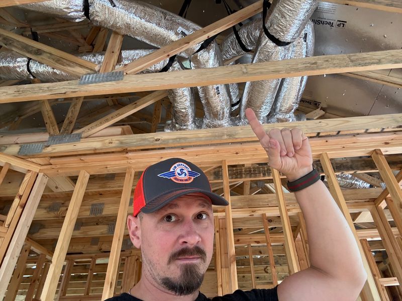 Air Support technician pointing to insulated flex duct runs in new construction attic framing
