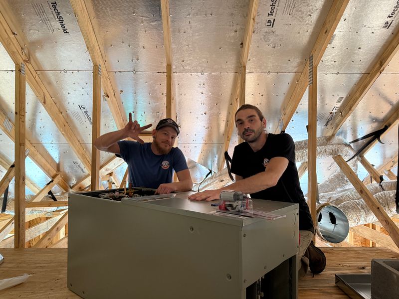 Two Air Support technicians installing an air handler unit in a new construction attic