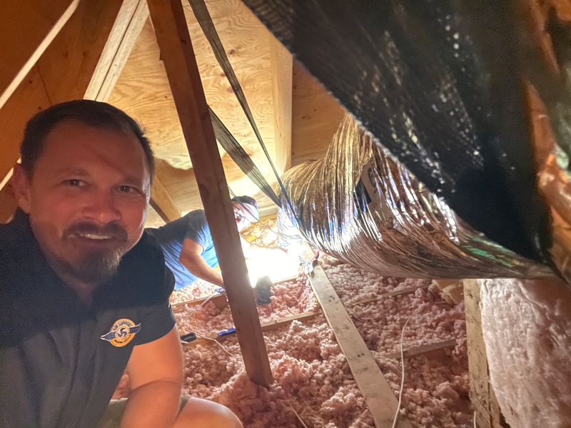 Air Support technician in an attic crawl space next to insulated ductwork with pink insulation