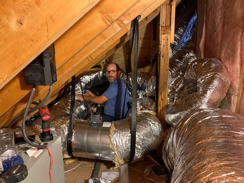 Air Support technician inspecting flex duct connections in an attic with insulated ductwork