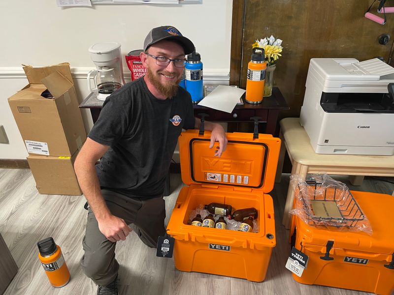 Air Support technician with branded orange Yeti coolers and water bottles at the office
