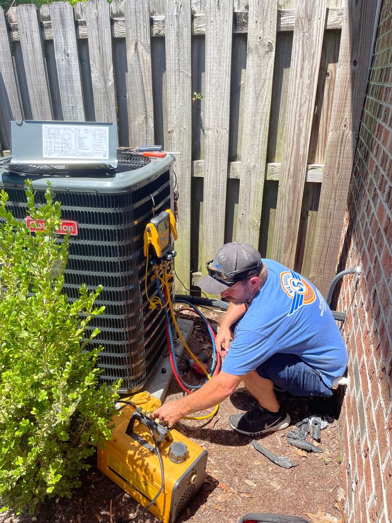 Air Support technician performing diagnostics on an outdoor AC condenser with refrigerant hoses
