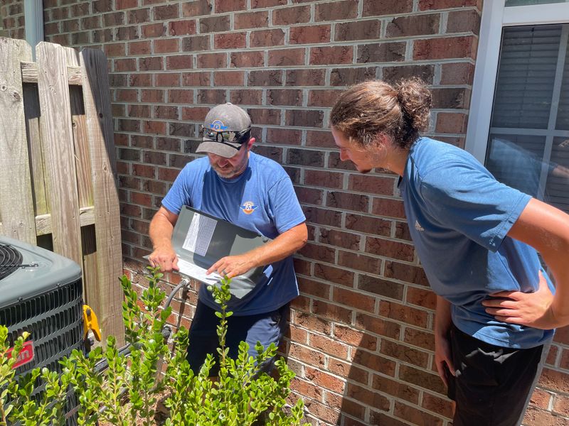 Two Air Support technicians reviewing technical specifications next to an outdoor AC unit