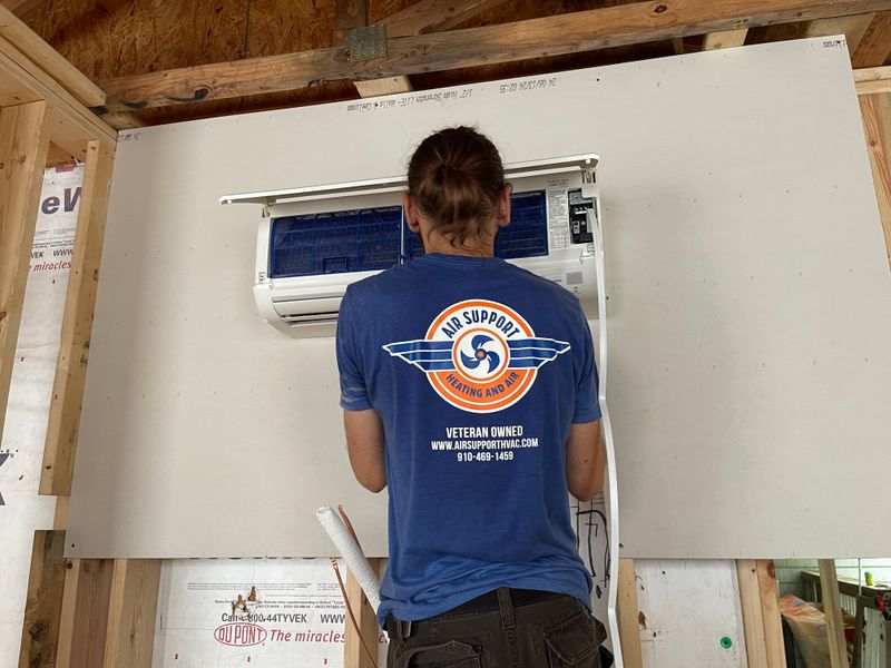 Air Support technician mounting a ductless mini-split indoor unit on a wall in new construction
