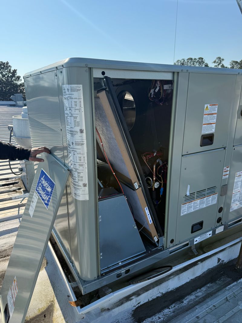 Technician working on an American Standard commercial rooftop unit with panels open
