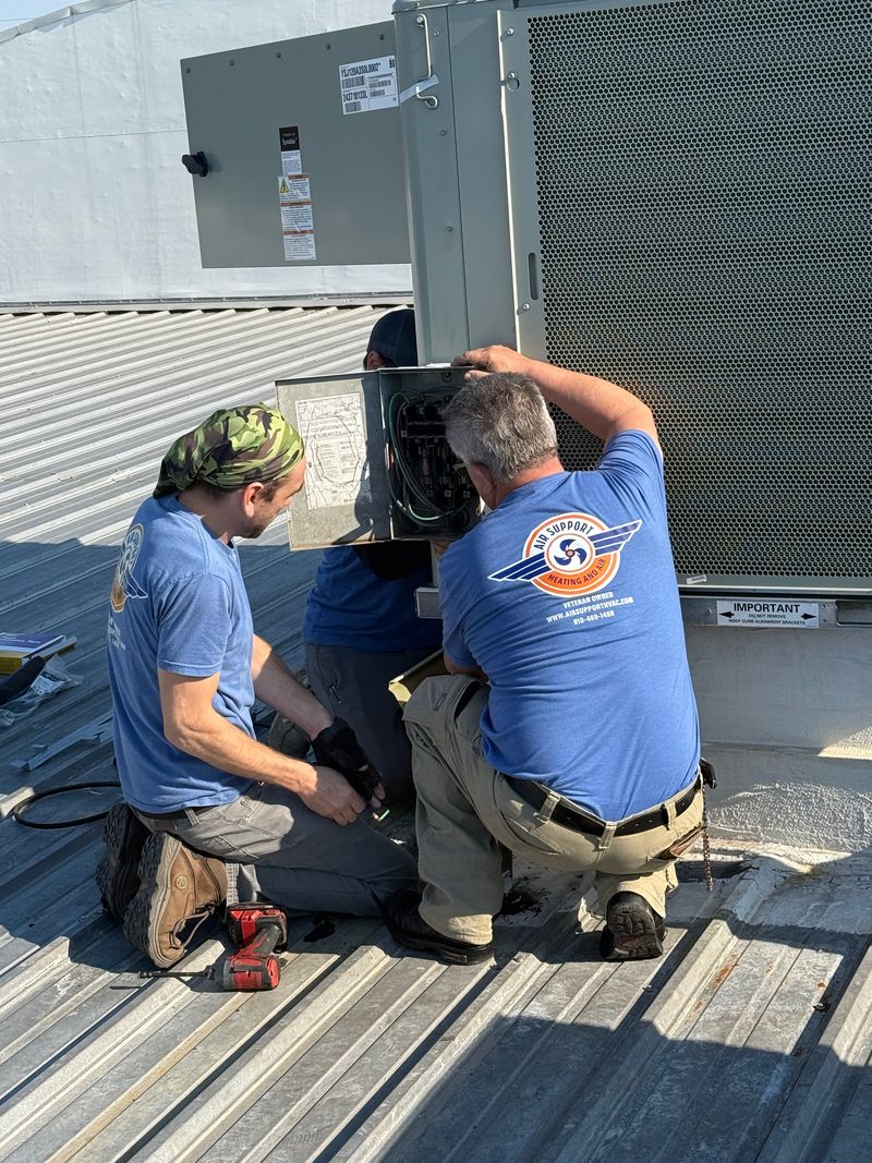 Two Air Support technicians working on rooftop commercial HVAC unit electrical connections